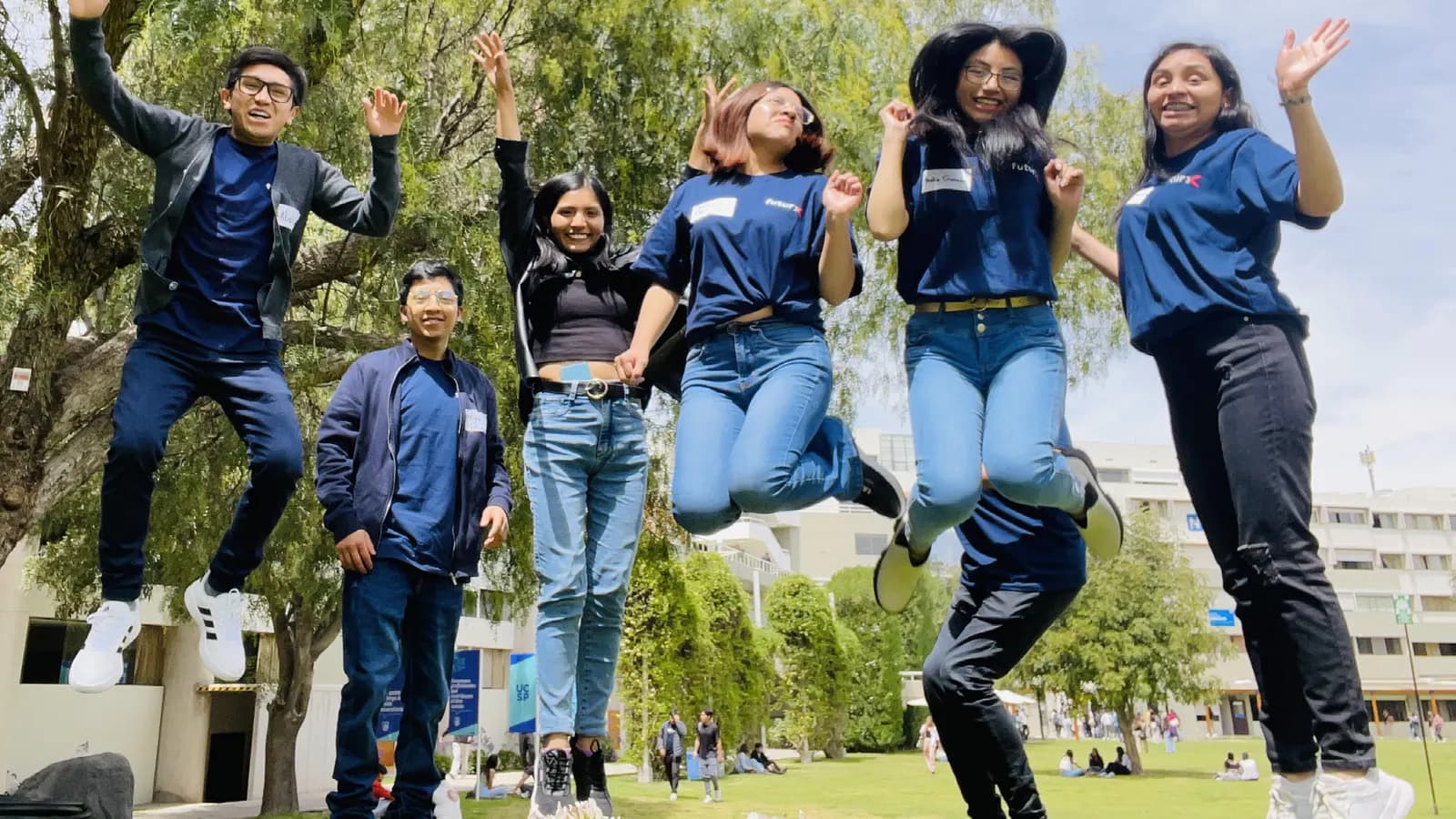 Seis integrantes de futurX saltando en el pasto del campus, con los brazos en alto.